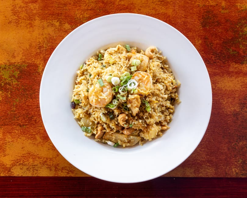 A white bowl filled with shrimp fried rice, garnished with green onions, on a rustic orange table.