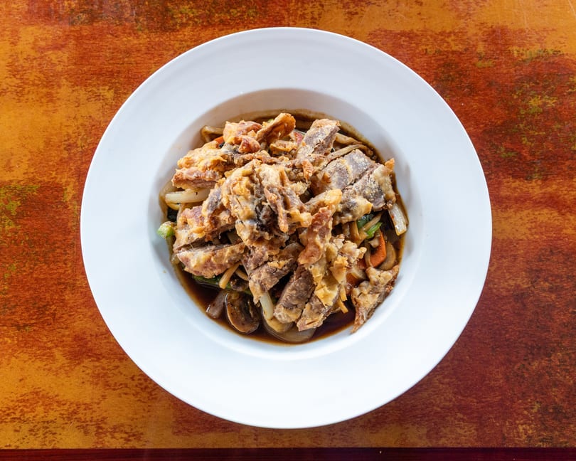 Top-down view of a white bowl filled with crispy fried soft-shell crab over noodles and vegetables.