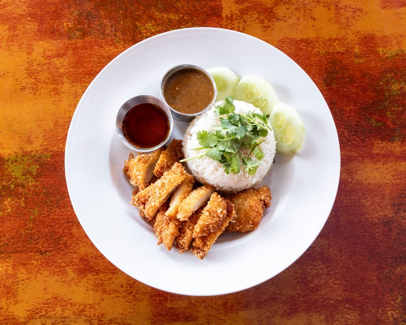 Crispy fried chicken, white rice with cilantro, cucumber slices, and two dipping sauces on a white plate.