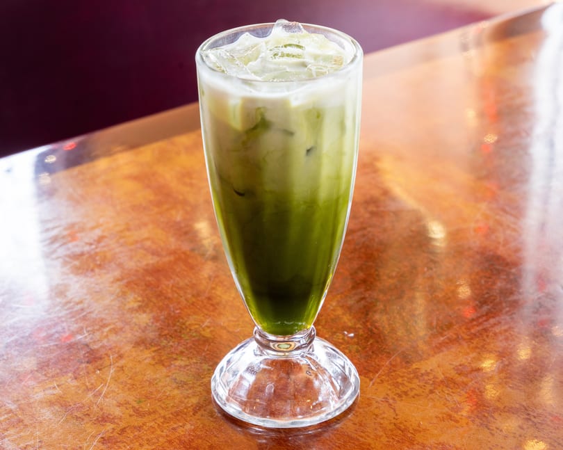 Iced matcha latte with a layer of white milk on top, served in a tall glass on a wooden table.